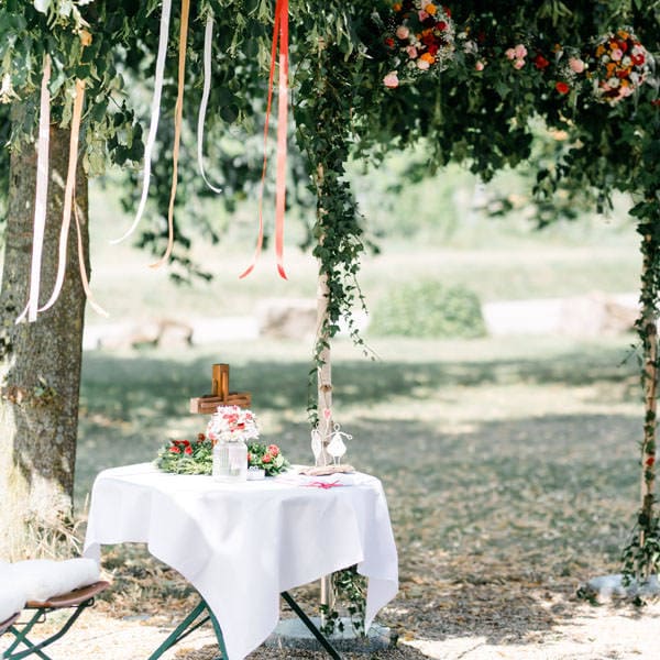 Ein Galerietisch mit Hochzeitsblumen und Dekorationsbändern unter einem Baum.