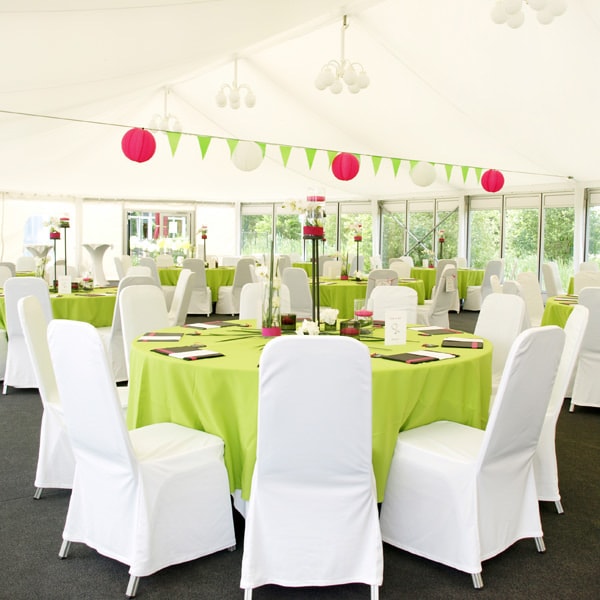 Eine Galerie mit grün-weißer Hochzeitsdekoration, inklusive weißen Tischen und Stühlen.