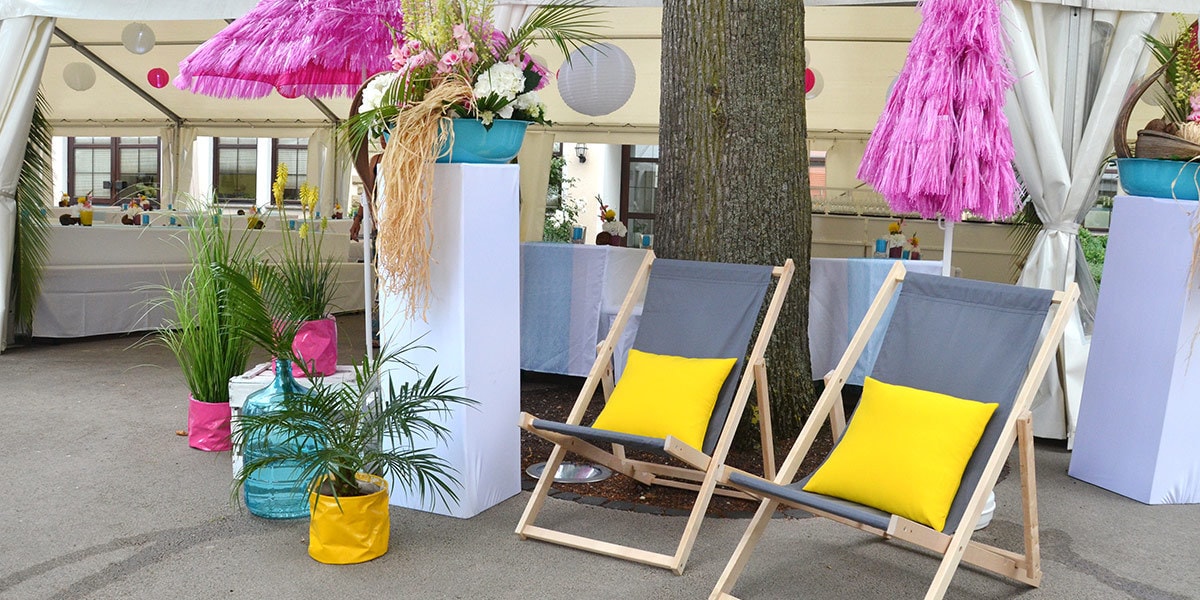 Ein Tisch mit Stühlen und Sonnenschirmen unter einem Zelt, dekoriert für Firmenveranstaltungen.