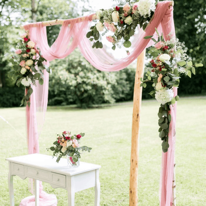 Beschreibung: Eine rosafarbene Hochzeitsarche mit Blumen und einem weißen Tisch in einer Galeriehochzeitdekoration.