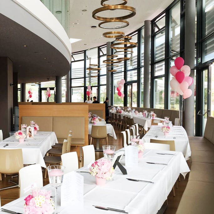 Ein großes Restaurant mit weißen Tischen und rosa Luftballons.