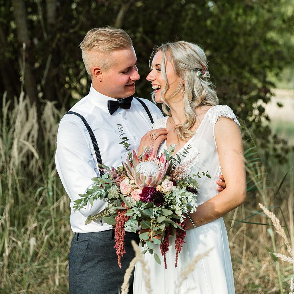 Eine lächelnde Braut und ein Bräutigam auf einem Feld mit hohem Gras, umgeben von der bezaubernden Hochzeitsdekoration der Galerie.