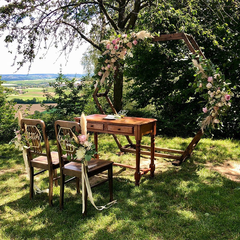 Inmitten eines blühenden Feldes schaffen ein elegant arrangierter Tisch und Stühle eine malerische Galerie für eine romantische Hochzeitsfeier. Die bezaubernde Dekoration verleiht dem Ganzen eine zauberhafte Note