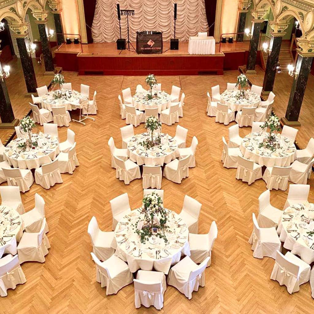 Eine Hochzeitsfeier in einem großen Saal mit weißen Tischen und Stühlen. Galerie