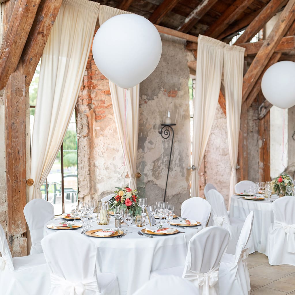 Beschreibung: Eine Hochzeitsfeier mit weißen Tischen und weißen Luftballons in einer Galerie.