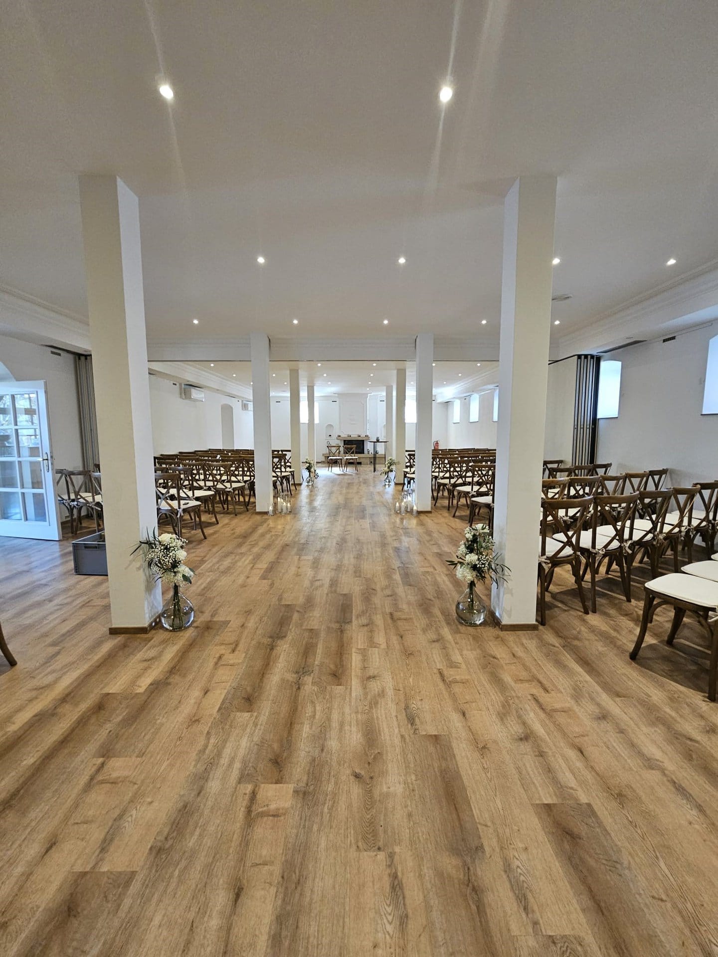 Der Innenraum von Schloss Michelfeld ist für eine Zeremonie mit Reihen brauner Holzstühle, weißen Säulen und Blumenarrangements entlang des Mittelgangs vorbereitet.