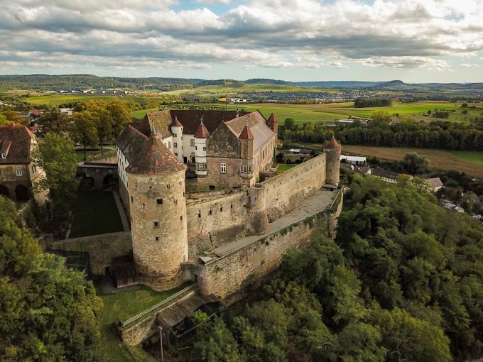 Luftaufnahme der historischen Stätte Burg Stettenfels, umgeben von üppigem Grün in einer ländlichen Landschaft unter einem bewölkten Himmel.