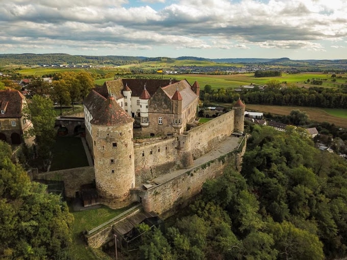 Luftaufnahme der historischen Stätte Burg Stettenfels, umgeben von üppigem Grün in einer ländlichen Landschaft unter einem bewölkten Himmel.