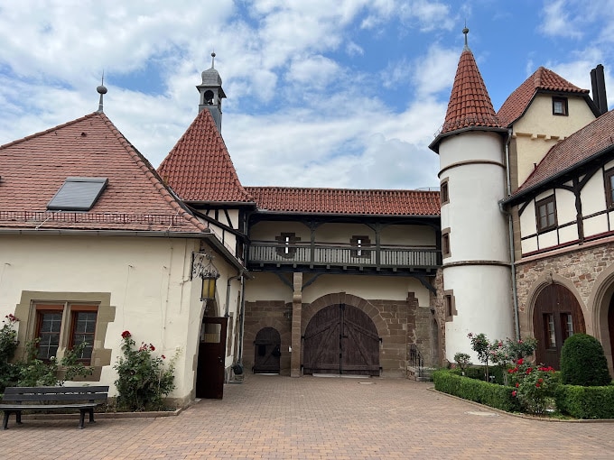 Innenhof eines Schlosses im europäischen Stil mit Holzbalkon und rot gedeckten Türmen, die die Orangerie umgeben.
