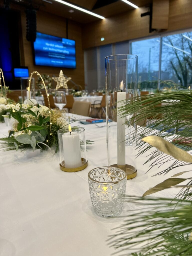 Elegante Bankett-Tischdekoration mit Kerzen, Blumendekorationen und einem blauen Präsentationsbildschirm im Hintergrund.