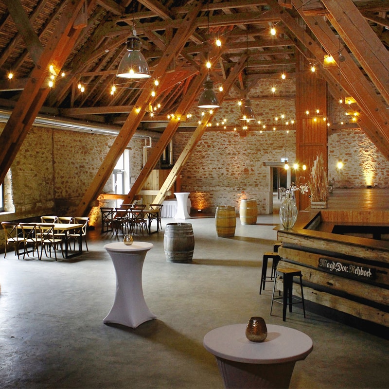 Rustikale Innenräume einer Scheune mit Lichterketten, Holzbalken und arrangierten Sitzgelegenheiten.