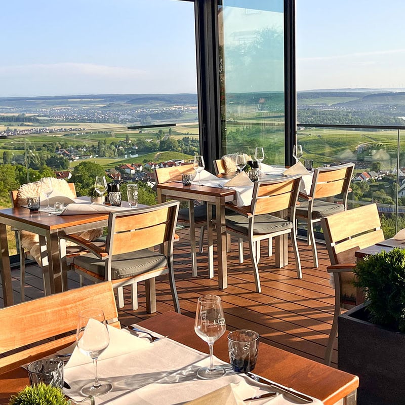 Essbereich im Freien mit malerischer Aussicht für eine Mahlzeit, mit Tischen mit Gläsern an verschiedenen Stellen und einer Landschaft im Hintergrund.