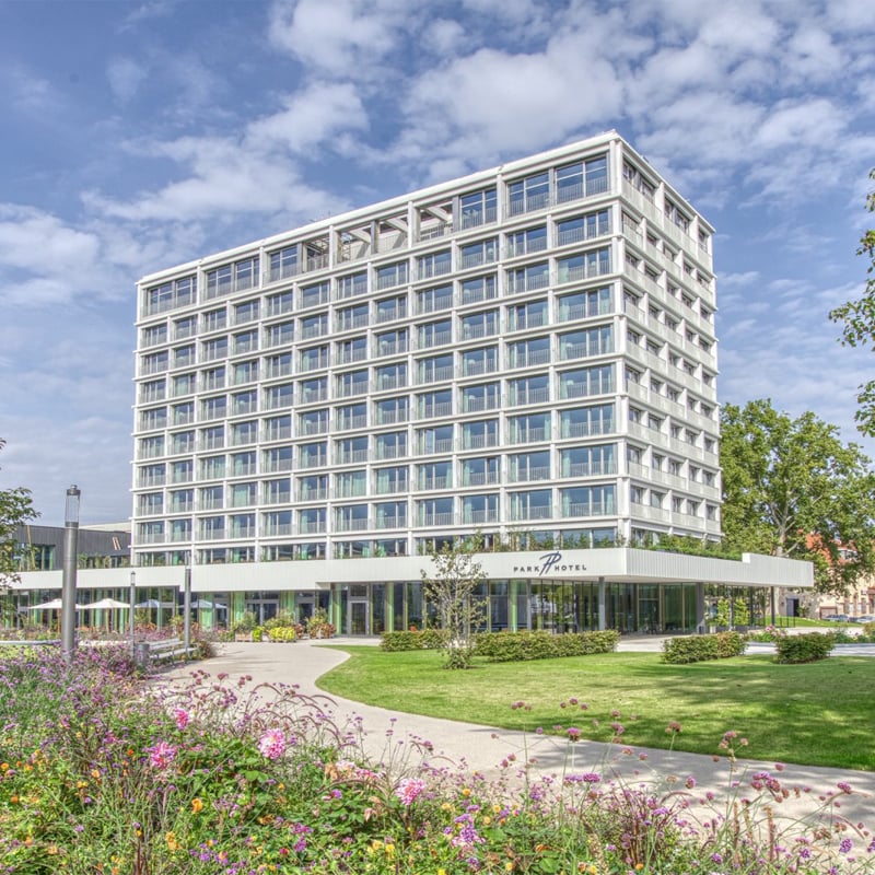 Modernes mehrstöckiges Gebäude mit Einzelhandelsflächen im Erdgeschoss, in bester Lage, umgeben von angelegten Gärten unter klarem Himmel.