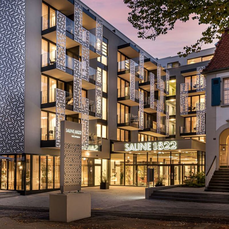 Modernes Geschäftsgebäude mit gemusterter Fassade, die in der Dämmerung beleuchtet wird und an verschiedenen Stellen mit der Aufschrift „Saline 1822“ versehen ist.