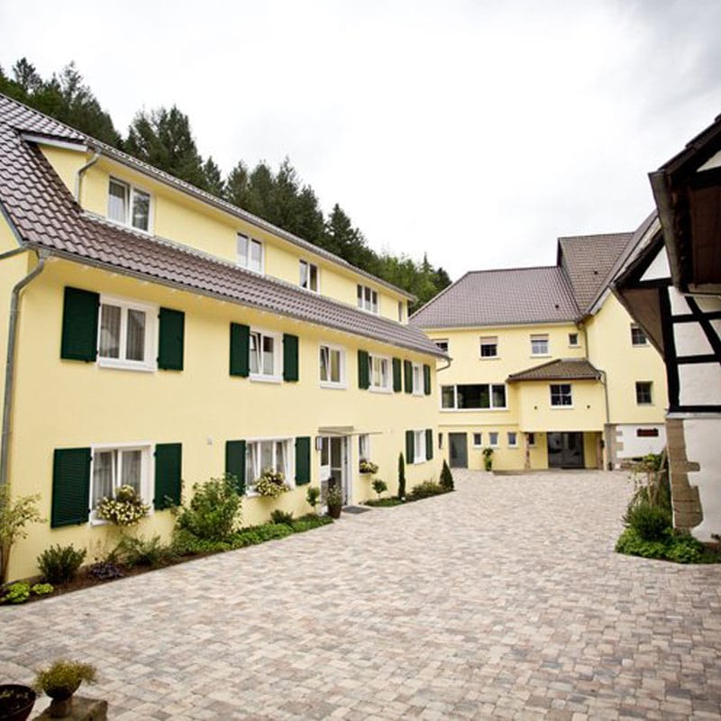 Blick auf den Innenhof eines gelben Gebäudes mit grünen Fensterläden in malerischer ländlicher Lage.