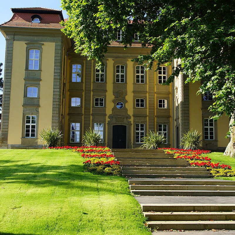 Klassisches Gebäude im europäischen Stil mit einem roten Blumenbeet und Steinstufen in einem üppig grünen Garten an verschiedenen Standorten.