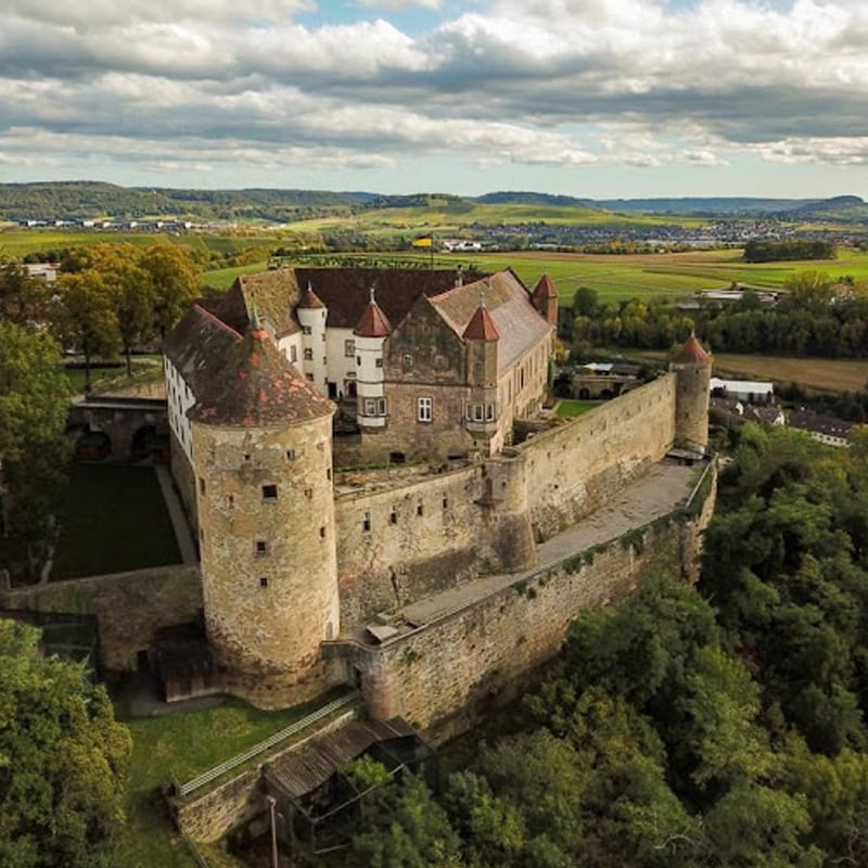 Luftaufnahme einer mittelalterlichen Burg mit Türmen und Umfassungsmauern inmitten einer grünen Landschaft an verschiedenen Standorten.