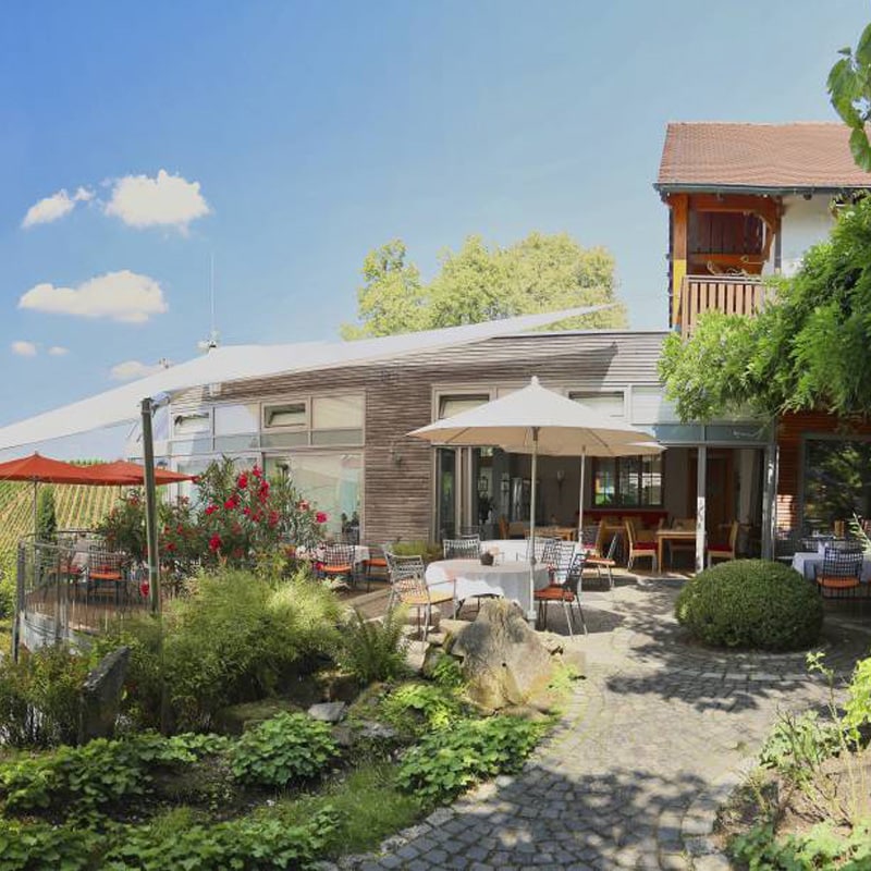 Essbereich auf der Terrasse eines Restaurants mit Sonnenschirmen und einem üppigen Garten unter klarem Himmel, perfekt für verschiedene Standorte.