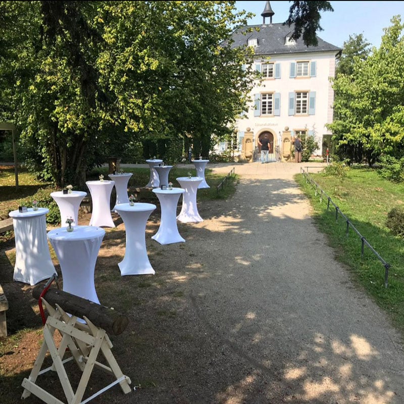 Outdoor-Event-Setup mit weiß gedeckten Cocktail-Tischen, das zu einem klassischen Gebäude an mehreren Standorten führt.