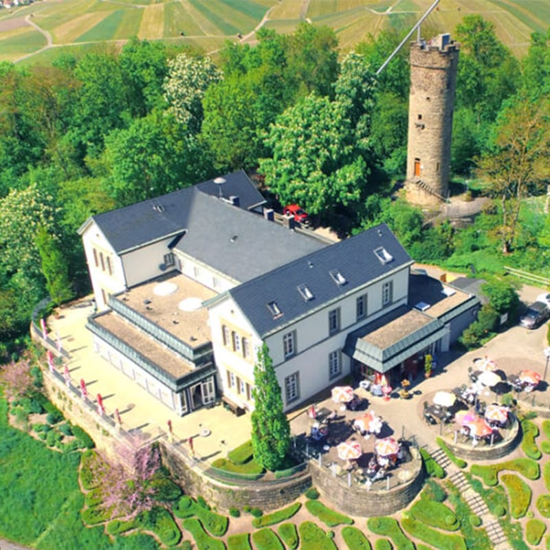 Luftaufnahme eines ländlichen Anwesens mit einem Steinturm, einem Sitzbereich im Freien und einer landschaftlich gestalteten Umgebung.