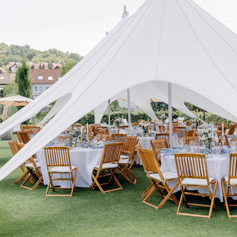 Eleganter Outdoor-Event-Aufbau mit weißen Zelten und an verschiedenen Stellen auf einer Rasenfläche aufgestellten Tischen und Stühlen.