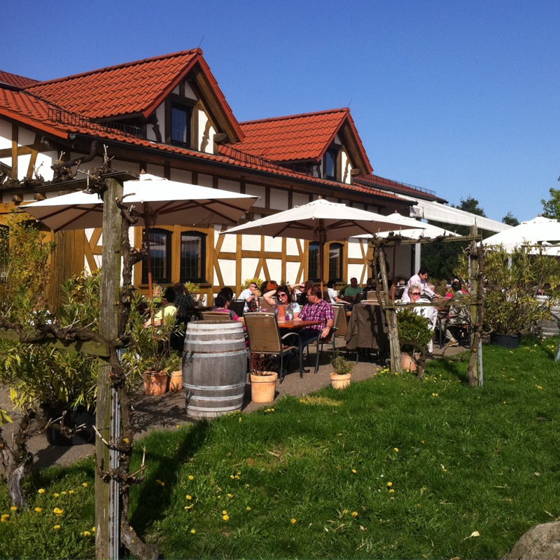 An einem sonnigen Tag speisen Gäste im Freien in einem Restaurant in traditioneller Fachwerkarchitektur.