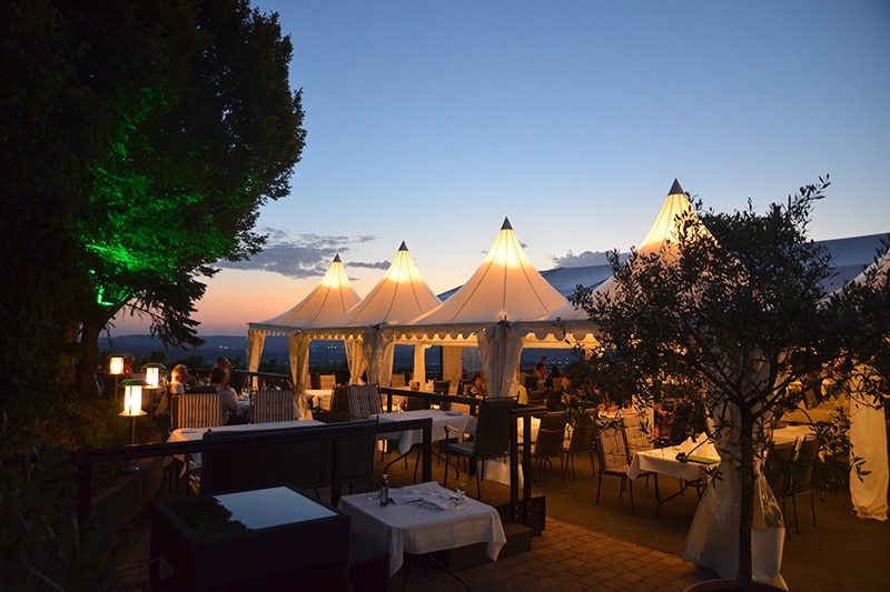 Freiluftrestaurant in der Abenddämmerung mit beleuchteten weißen Zelten, gedeckten Tischen und einem grün beleuchteten Baum beim Landgasthof Haigern.