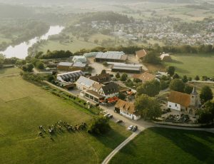 Luftaufnahme eines kleinen, ländlichen Dorfs mit Schäfers Michaelsbergkirche, gruppierten Gebäuden und umliegendem Ackerland neben einem gewundenen Fluss.