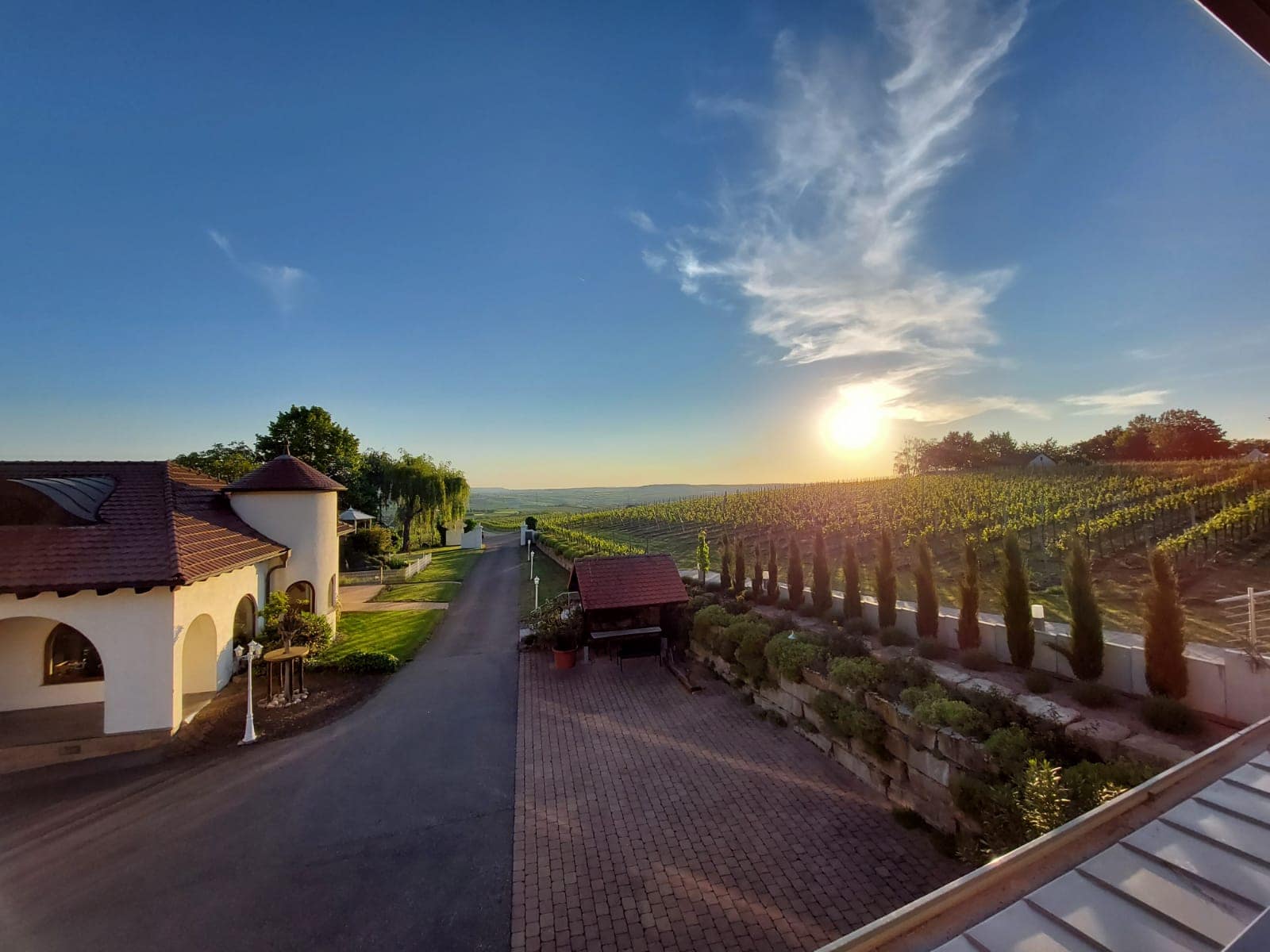 Sonnenuntergang über dem Familienweingut Kurz-Wagner mit klarem Himmel und Gebäuden auf der linken Seite.
